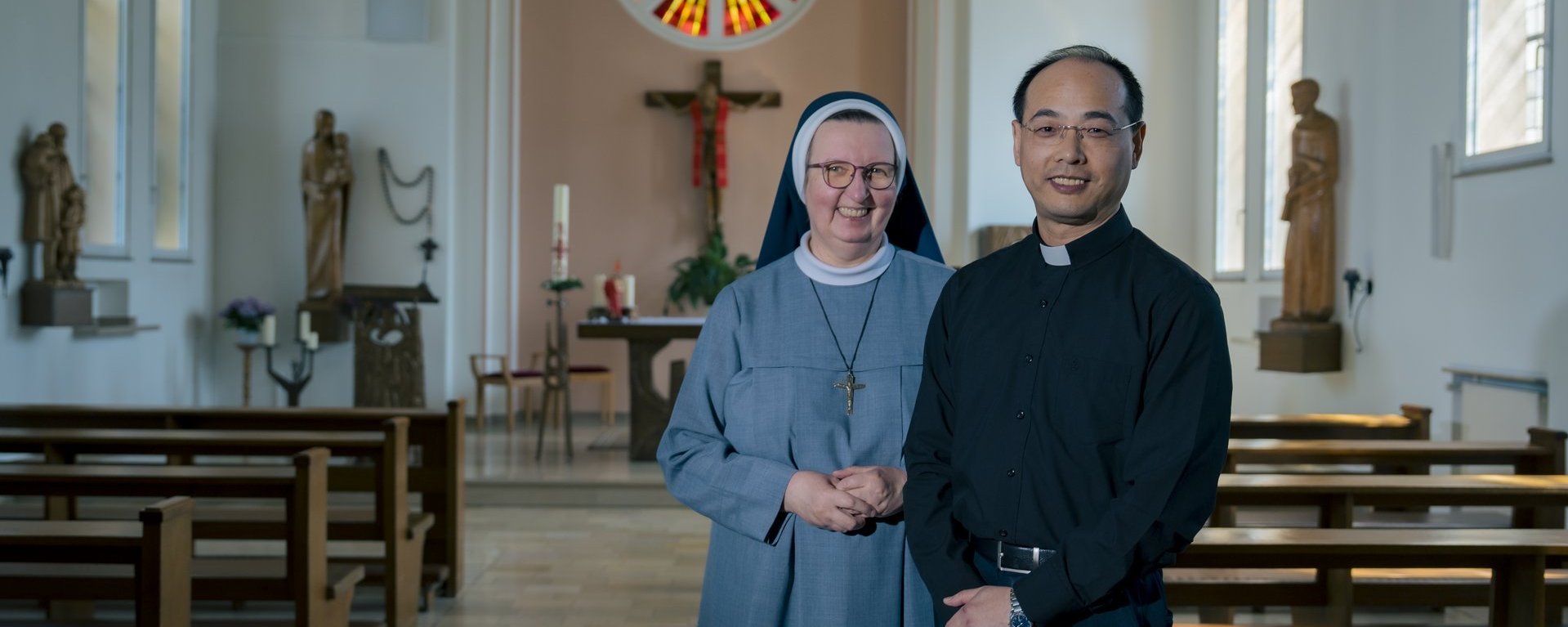 Der Hausgeistliche und eine Ordensschwester stehen in der Hauskapelle und lächeln in die Kamera.