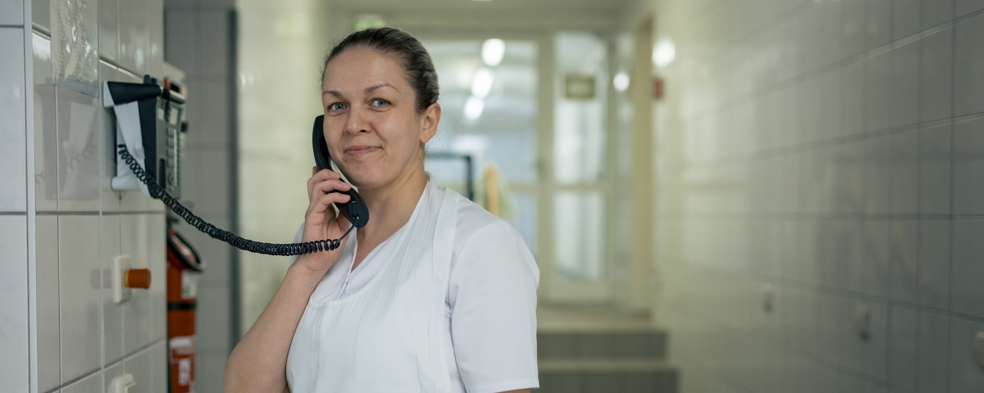 Eine Mitarbeitende hält den Telefonhörer ans Ohr und lächelt in die Kamera.